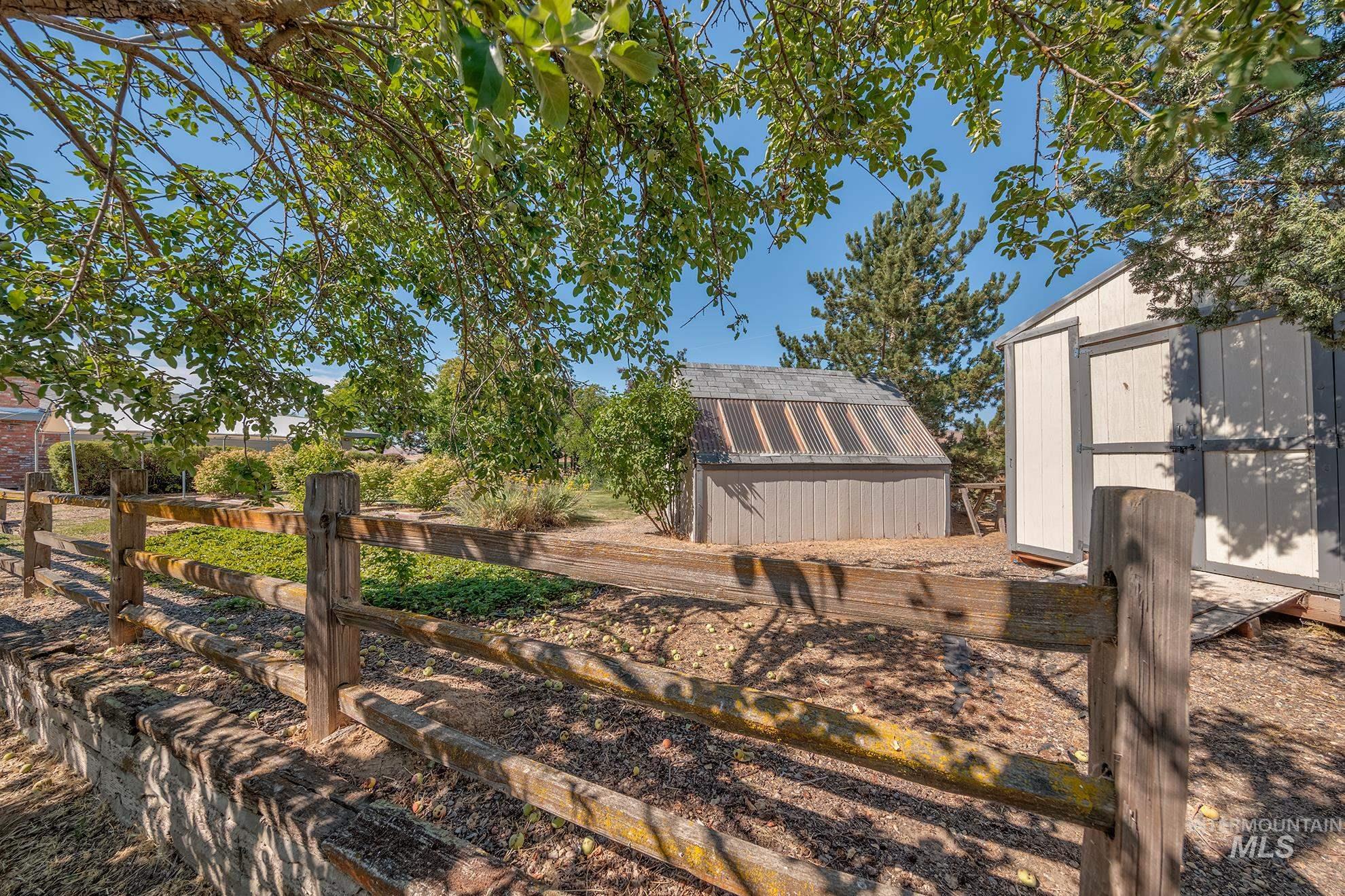 1493 Cove Road Weiser, ID 83672 - Photo 46 of 50 Split rail fence with stone base, two utility sheds, and mature trees