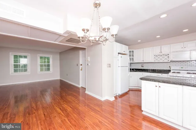 a kitchen with stainless steel appliances granite countertop a refrigerator a sink dishwasher a stove and white cabinets with wooden floor