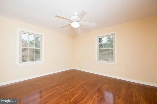 an empty room with wooden floor fan and windows
