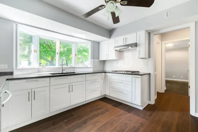 a kitchen with stainless steel appliances granite countertop white cabinets a stove a sink and a large window