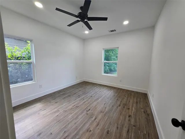 an empty room with wooden floor fan and windows