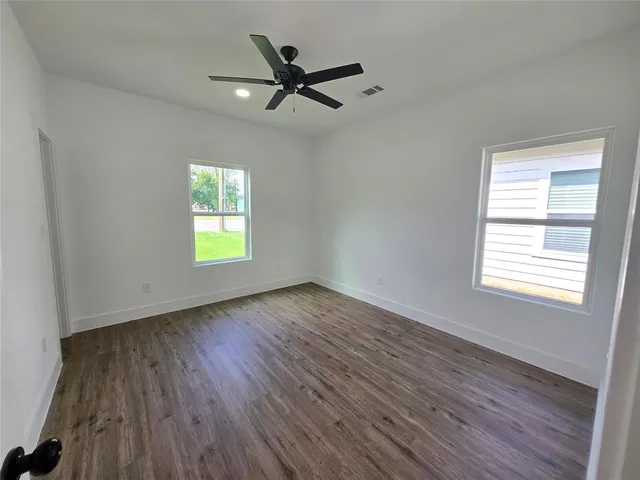 a view of a livingroom with a hardwood floor a ceiling fan and windows