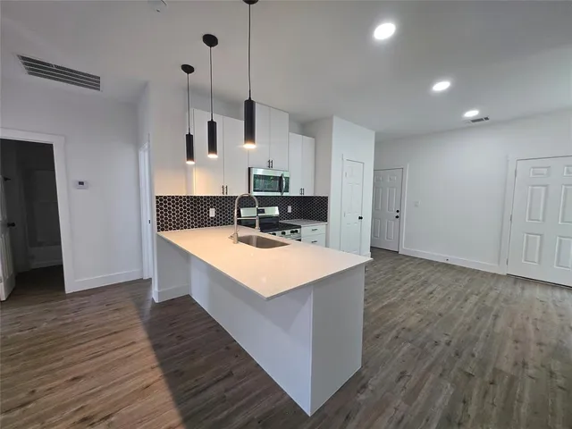 a kitchen with stainless steel appliances a sink a stove a refrigerator and white cabinets with wooden floor