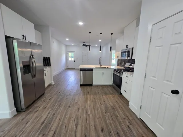 a large kitchen with stainless steel appliances a refrigerator a sink dishwasher a stove and white cabinets with wooden floor