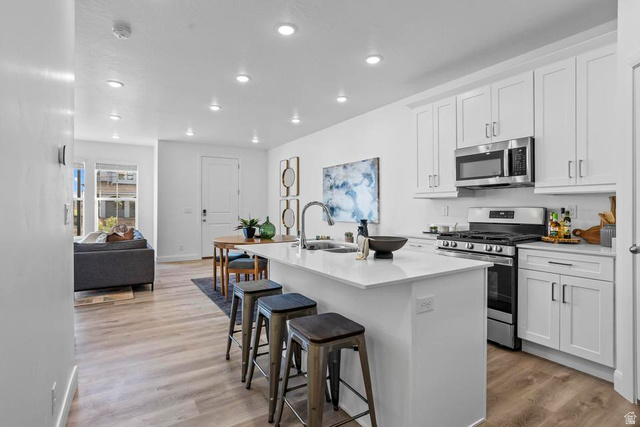 488 West Greenstone Pl Street, Unit 1010 St. George, UT 84790 - Photo 16 of 34 Open-concept kitchen featuring an island with seating, white shaker cabinetry, stainless steel appliances, and wood-finish flooring