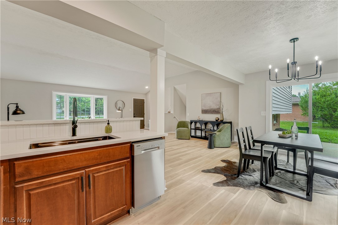 646 Ledge Road Macedonia, OH 44056 - Photo 8 of 28 Kitchen island with a built-in sink and stainless steel dishwasher, light wood-finish flooring, white shiplap paneling, a dining area with a modern chandelier, and sliding glass doors to the exterior