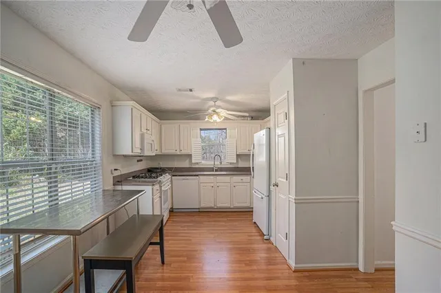 a kitchen with stainless steel appliances granite countertop a refrigerator a sink dishwasher a stove and white countertops with wooden floor