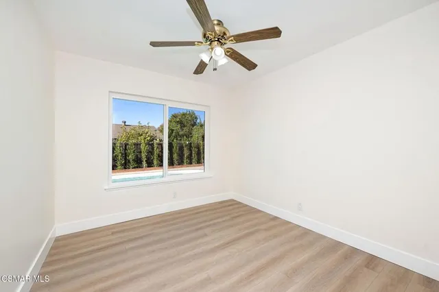 an empty room with wooden floor fan and windows