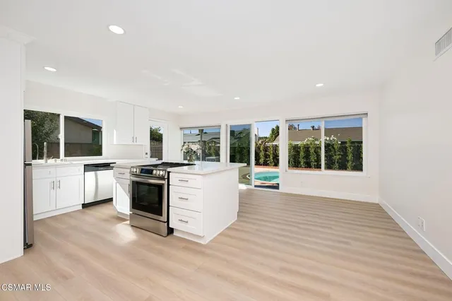 a large white kitchen with stainless steel appliances kitchen island granite countertop a stove and a large window