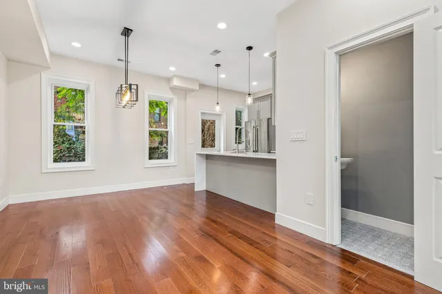 a view of an empty room with wooden floor and a kitchen