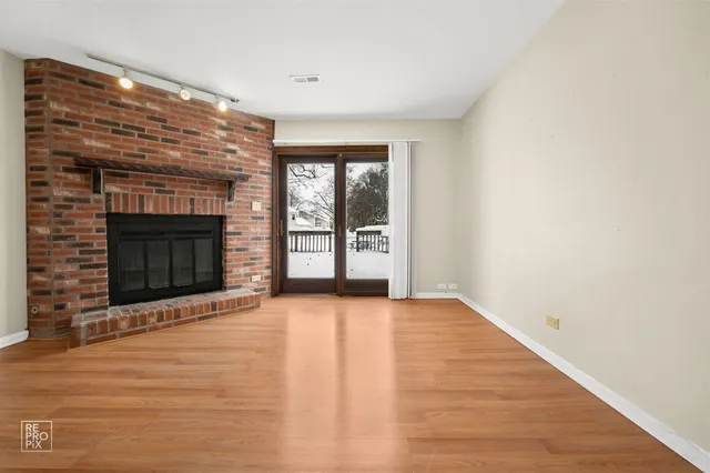a view of an empty room with wooden floor fireplace and a window