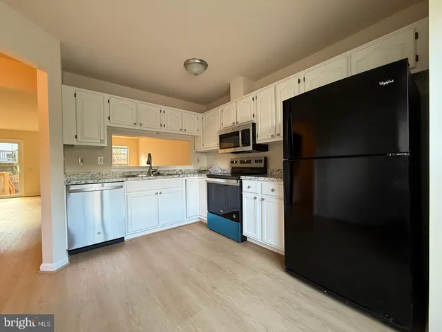 a kitchen with a refrigerator a sink dishwasher and a stove top oven with white cabinets