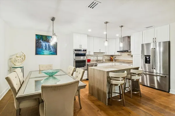 a kitchen with stainless steel appliances granite countertop a refrigerator a stove a sink a dining table and chairs with wooden floor