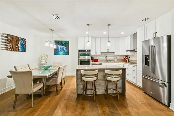 a kitchen with stainless steel appliances granite countertop a dining table chairs refrigerator and sink