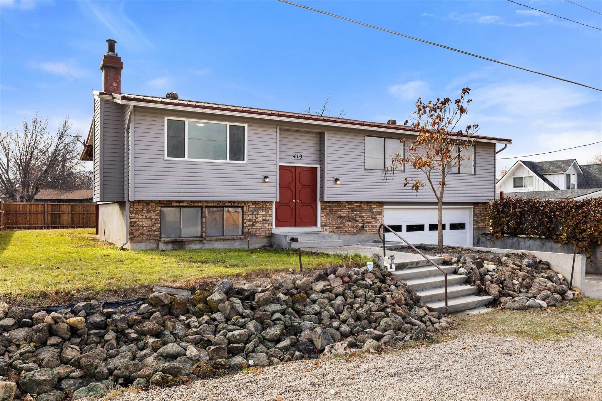 Raised ranch featuring an attached garage, a chimney, brick siding, and driveway