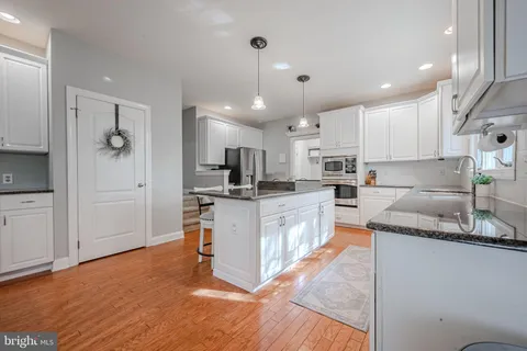 a large kitchen with stainless steel appliances kitchen island granite countertop a stove a sink a refrigerator and white cabinets with wooden floor