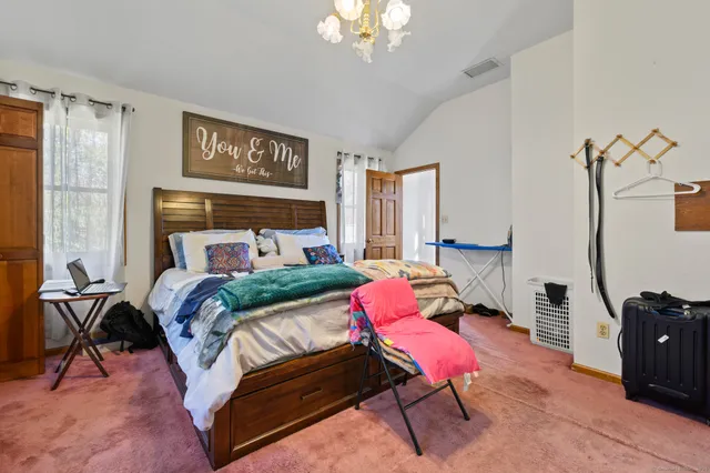 a bedroom with a bed a chair and potted plant on the dresser