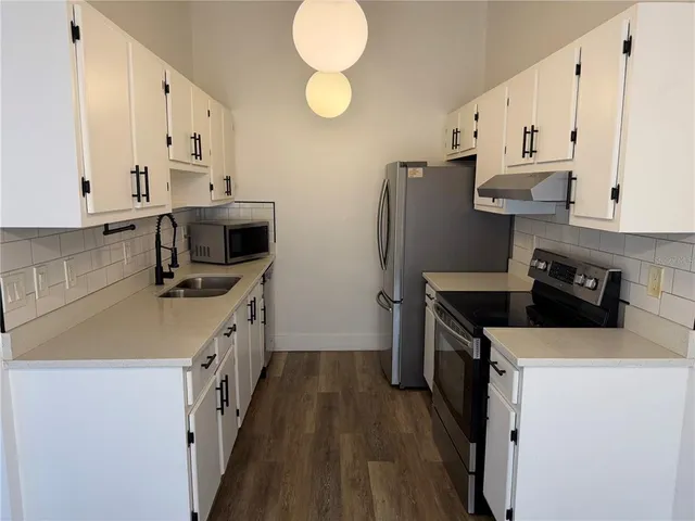 a kitchen with cabinets stainless steel appliances a sink and wooden floor