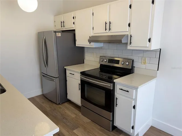 a kitchen with stainless steel appliances granite countertop a refrigerator a stove a sink and white cabinets