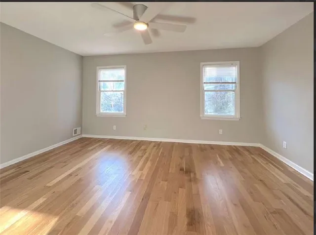 an empty room with wooden floor window and ceiling fan