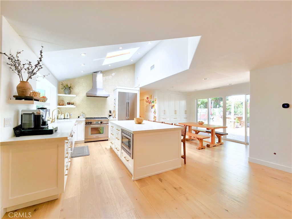 a large white kitchen with stainless steel appliances granite countertop a couch and a large window