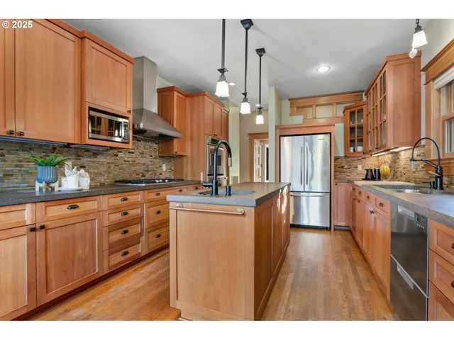 a kitchen with stainless steel appliances kitchen island granite countertop a refrigerator a oven a sink dishwasher and wooden cabinets with wooden floor