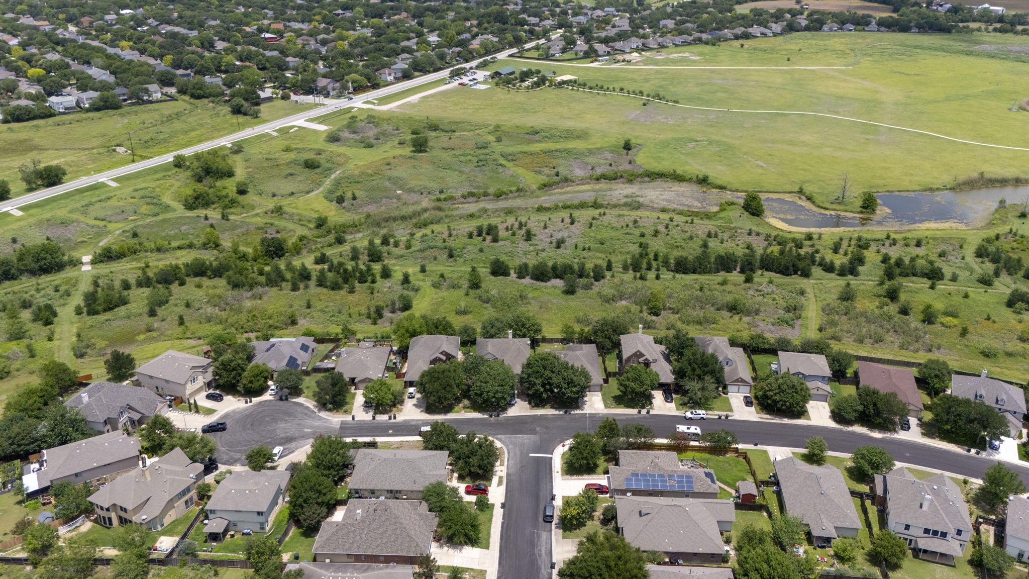 454 Fall Circle Kyle, TX 78640 - Photo 39 of 39 An aerial panorama reveals a residential enclave bordering a verdant landscape with tranquil pond features.