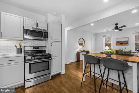 a kitchen with stainless steel appliances kitchen island granite countertop a stove a sink dishwasher and white cabinets with wooden floor