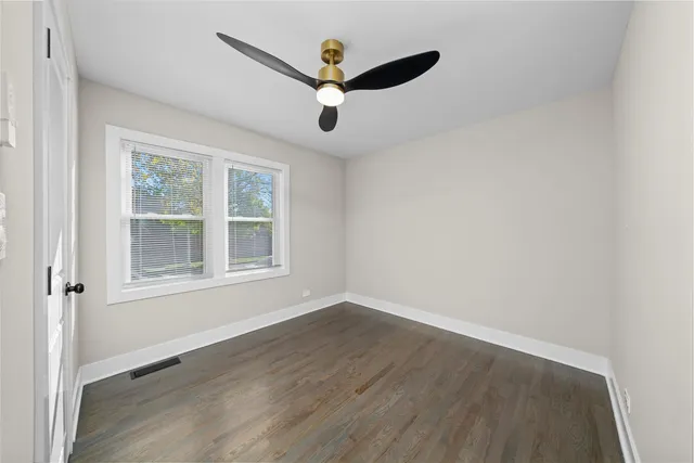 an empty room with wooden floor ceiling fan and windows