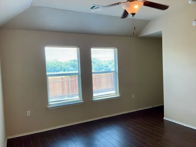 an empty room with a chandelier fan and wooden floor