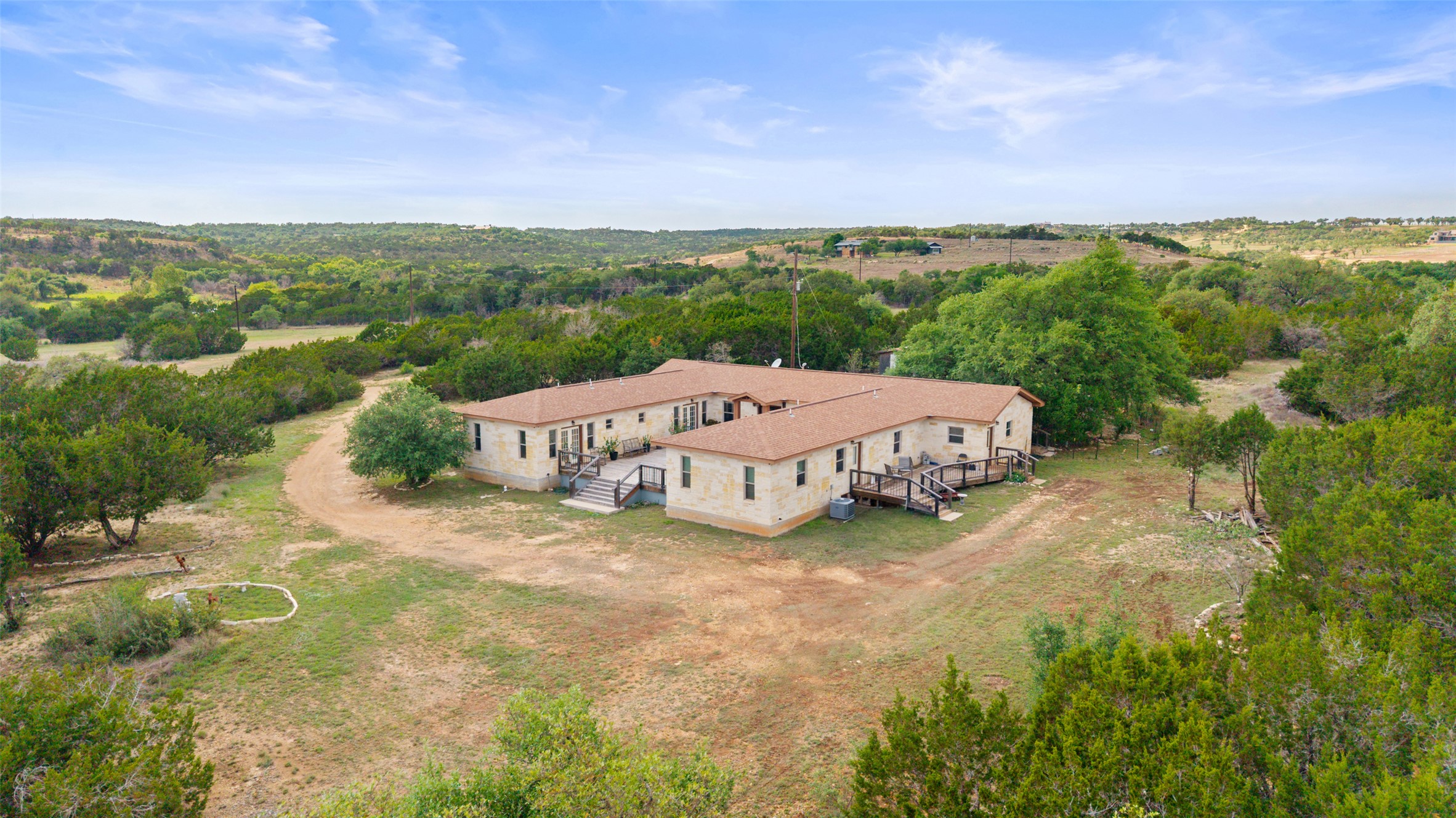 Expansive property featuring a single-story residence with a light-colored stone exterior and brown shingle roofing