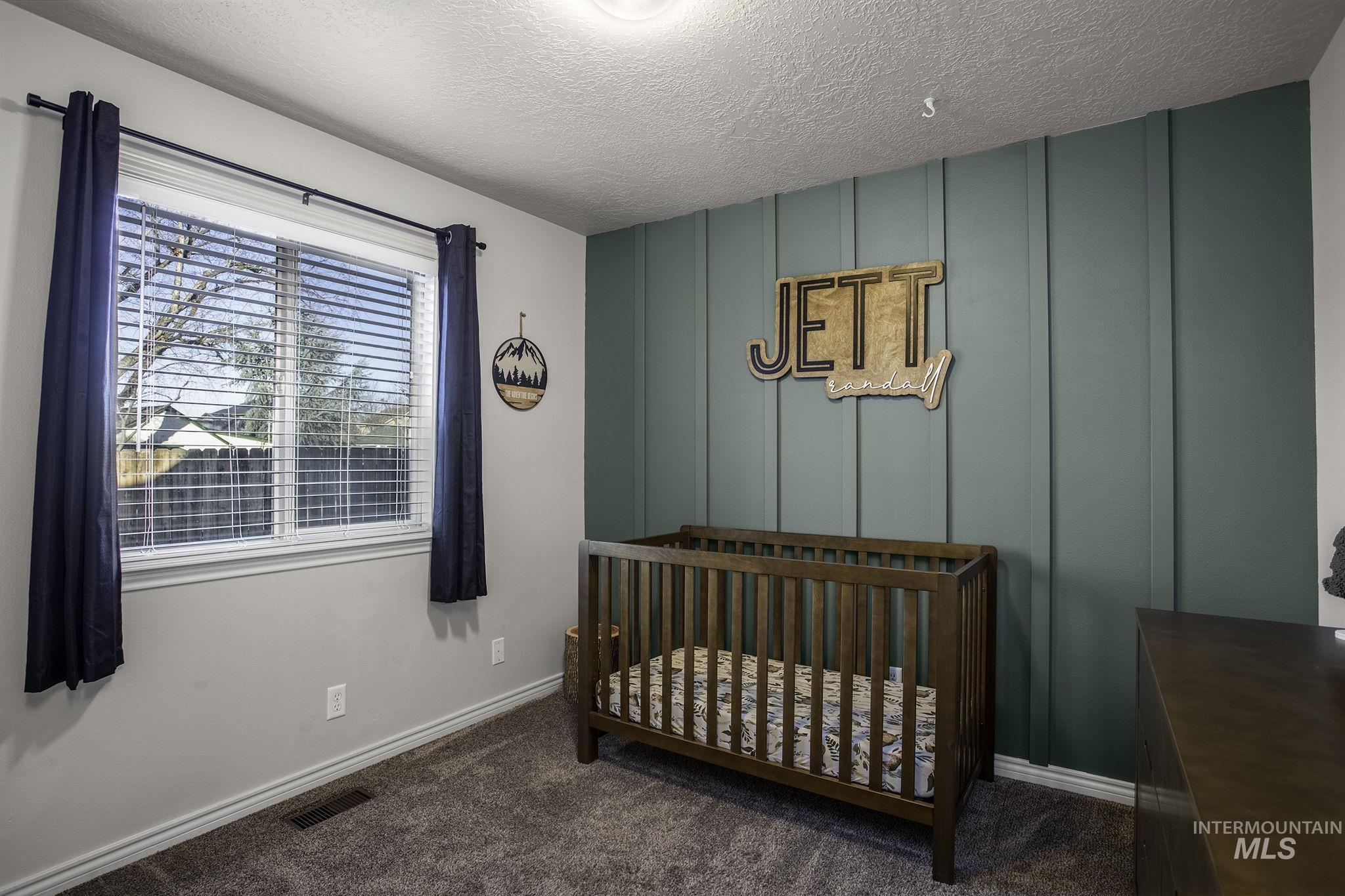 2217 East Satterfield Street Meridian, ID 83646 - Photo 17 of 33 Bedroom featuring a decorative wall, a crib, dark colored carpet, and a textured ceiling