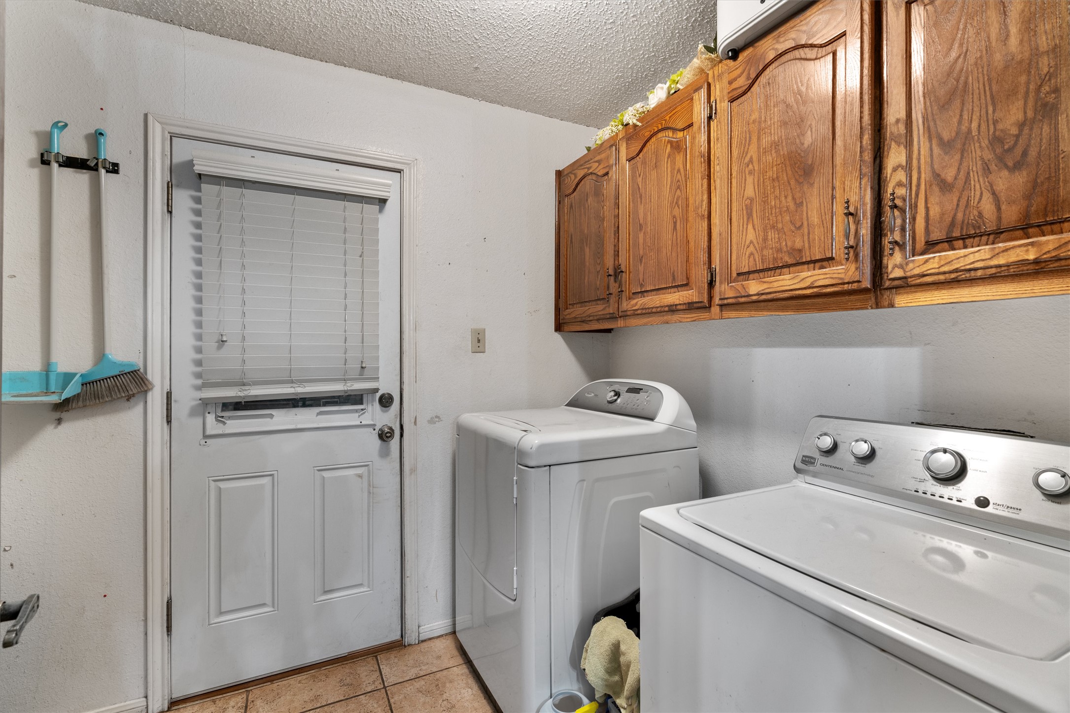 401 Drake Lane Taylor, TX 76574 - Photo 24 of 31 Laundry area featuring a utility door with integrated blinds, upper wood-finish cabinetry, and tiled flooring