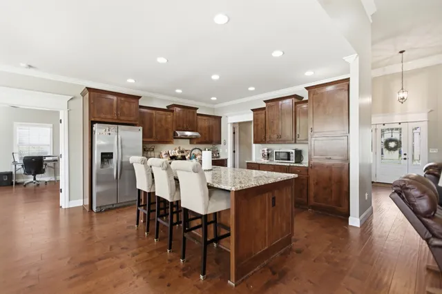 a kitchen with stainless steel appliances kitchen island granite countertop a refrigerator a stove a sink a dining table and chairs with wooden floor