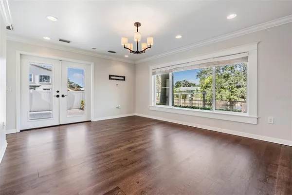 an empty room with wooden floor chandelier and windows