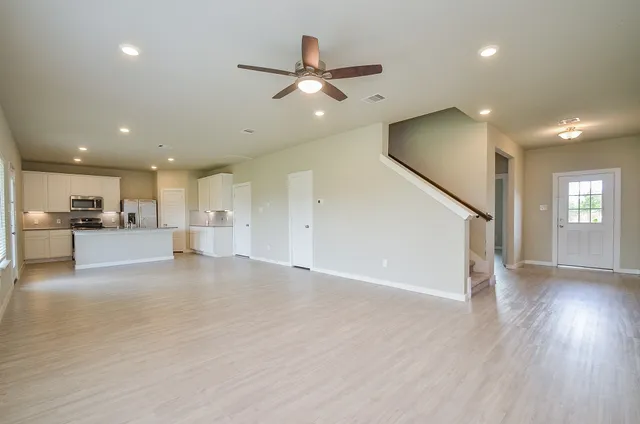 a view of an empty room and kitchen with wooden floor and a ceiling fan