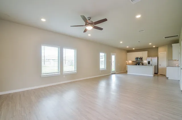 a view of an empty room with a kitchen and wooden floor