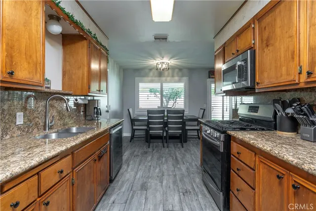 a kitchen with granite countertop a stove a sink and dishwasher wooden cabinets with wooden floor