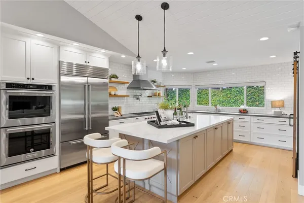 a kitchen with stainless steel appliances kitchen island granite countertop a refrigerator a sink a dining table and chairs with wooden floor