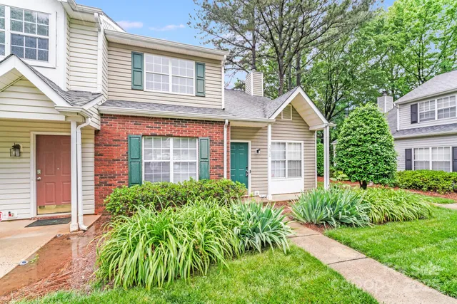 a view of a brick house with a large windows plants and large trees