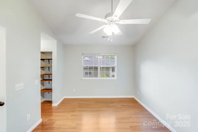 an empty room with wooden floor chandelier fan and windows