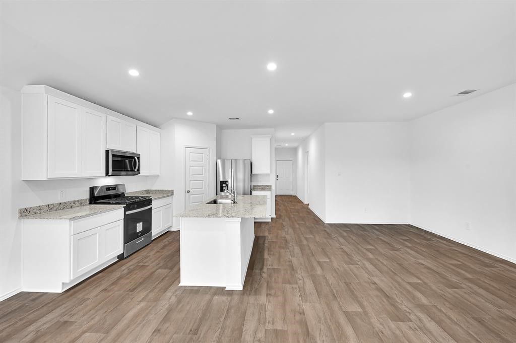 31006 Brightwell Bend Fulshear, TX 77441 - Photo 9 of 47 a open kitchen with kitchen island a stove top oven a sink dishwasher a refrigerator and white cabinets with wooden floor