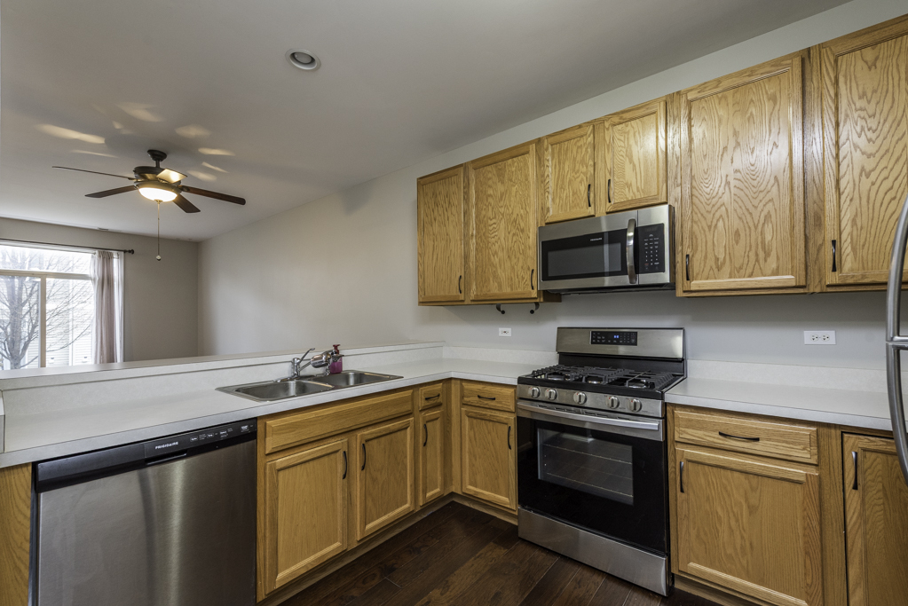 2879 Falling Waters Drive, Unit 2879 Lindenhurst, IL 60046 - Photo 8 of 30 a kitchen with stainless steel appliances granite countertop a sink dishwasher stove and microwave with wooden cabinets