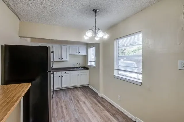 a kitchen with granite countertop a refrigerator a sink dishwasher a stove and white cabinets with wooden floor