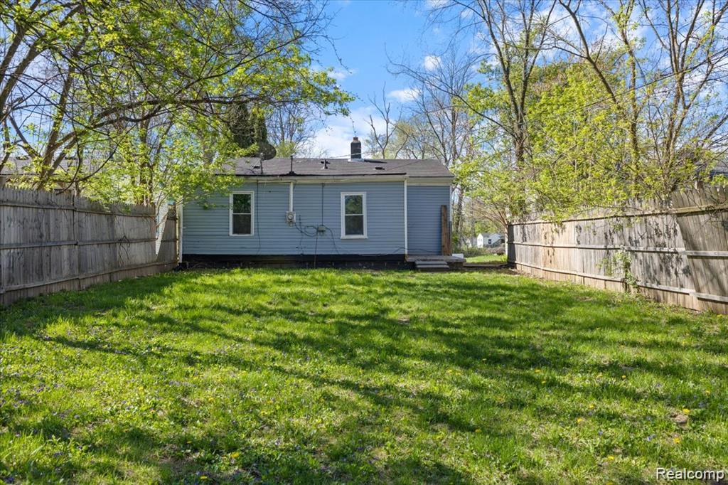 26076 Colgate Street Inkster, MI 48141 - Photo 21 of 24 Fenced backyard featuring a grassy lawn, mature trees, and a light blue exterior