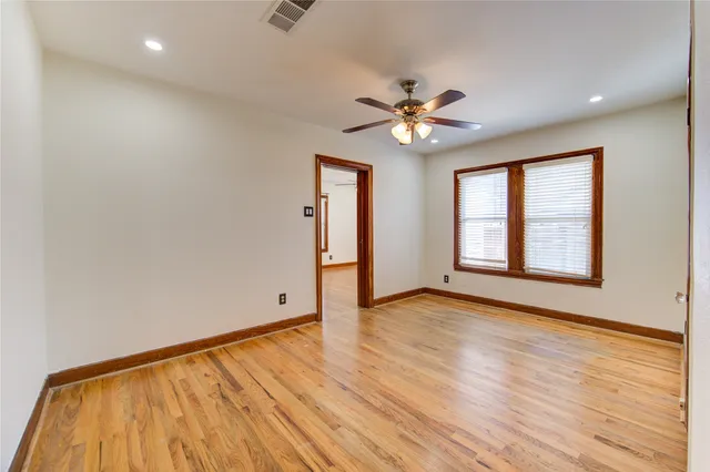 an empty room with wooden floor chandelier fan and windows