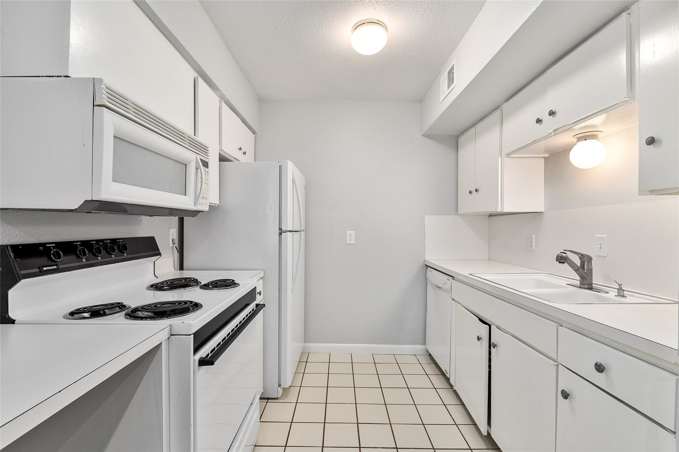 2408 Longview Street, Unit 113 Austin, TX 78705 - Photo 8 of 23 Kitchen featuring white appliances, light countertops, white cabinets, a textured ceiling, and light tile patterned floors