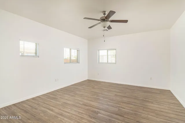 an empty room with wooden floor fan and windows