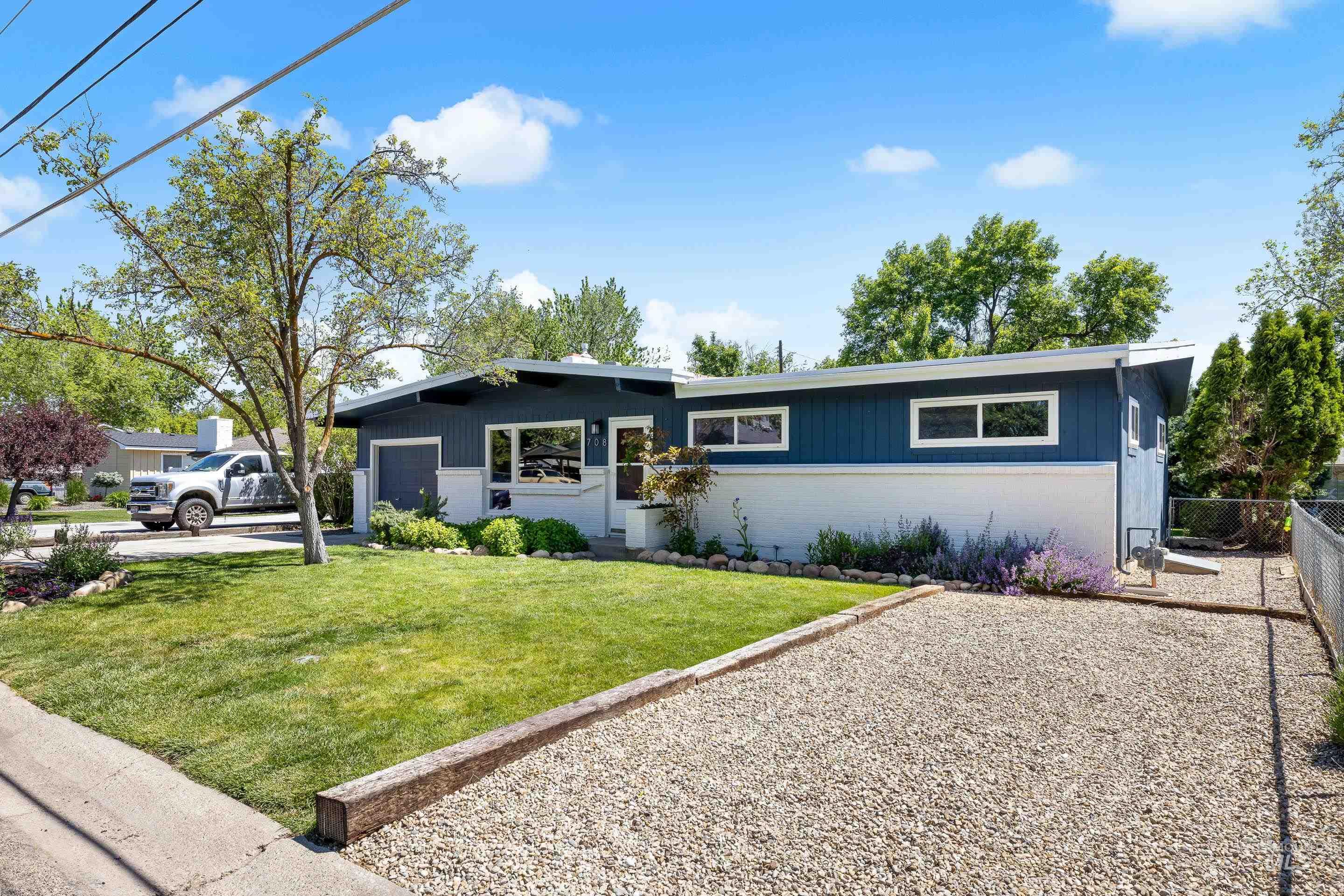 708 South Phillippi Street Boise, ID 83705 - Photo 22 of 25 Modern split-level exterior featuring blue and white siding, an attached garage, a pea gravel driveway, a manicured front lawn, and mature landscaping