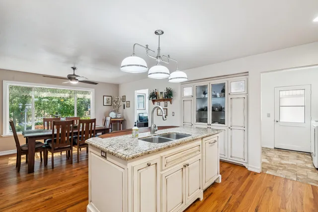a kitchen with granite countertop a stove a sink a dining table and chairs with wooden floor